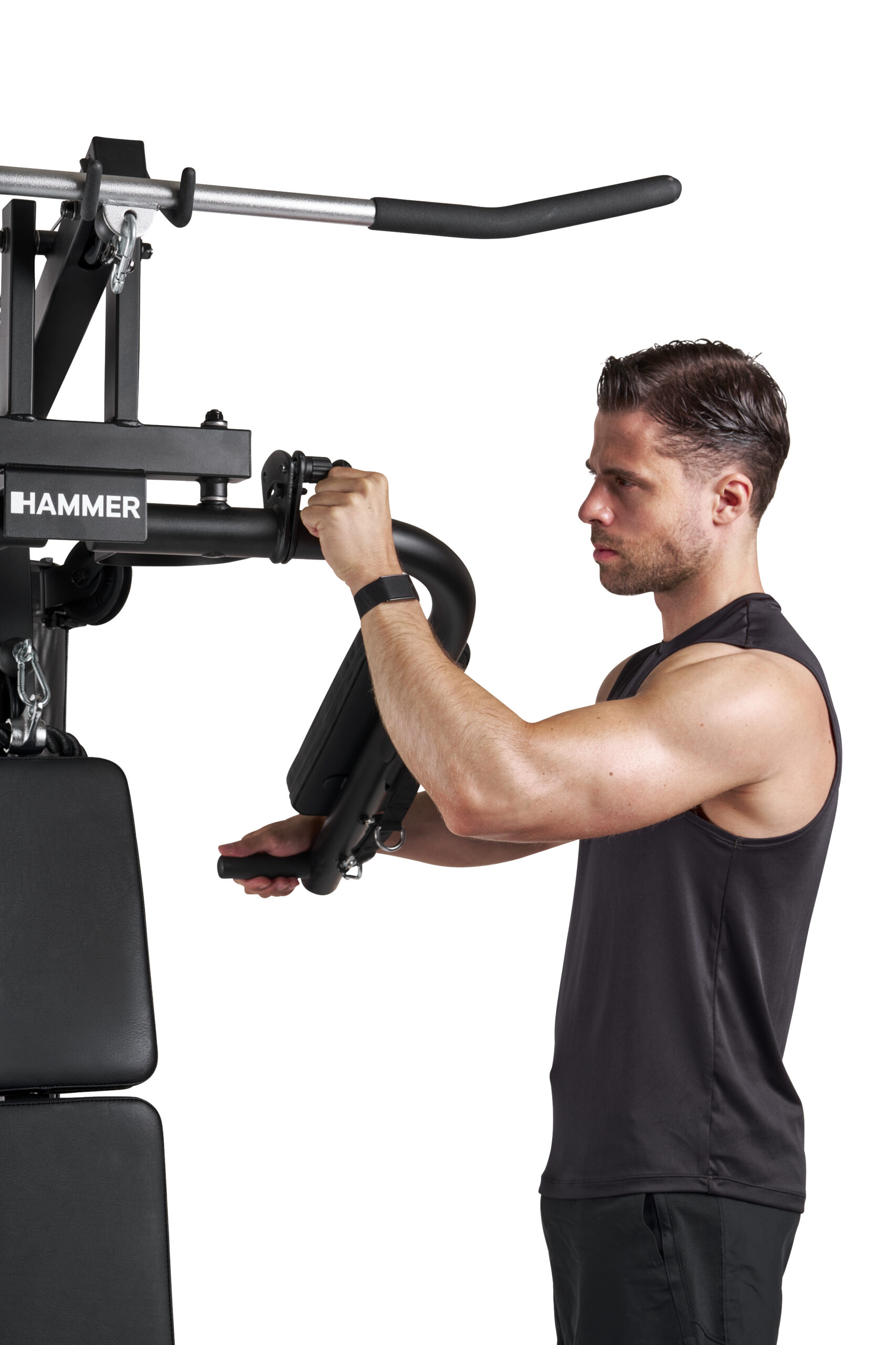 Man in a black sleeveless shirt uses a Hammer Strength gym machine, gripping handles for an upper-body exercise.
