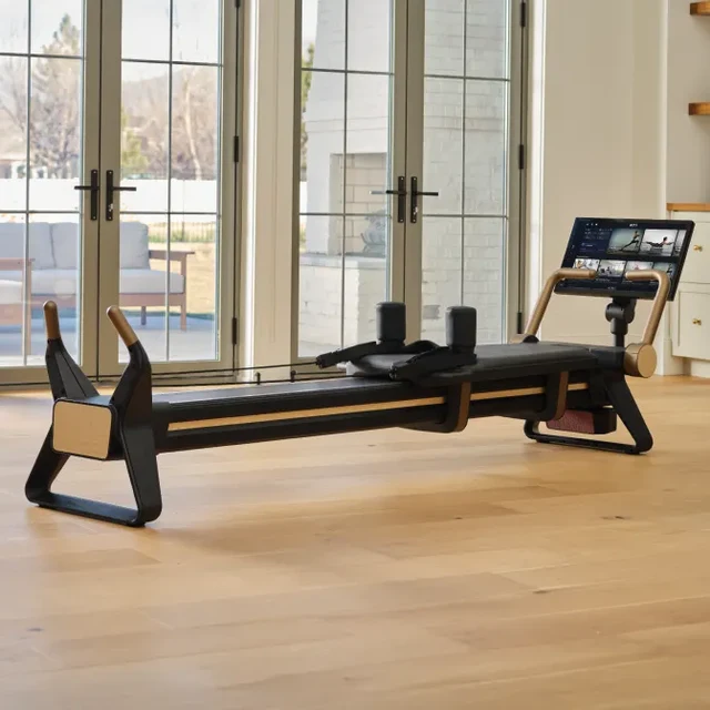 Pilates reformer machine with black upholstery in a bright home gym, large glass doors in the background.