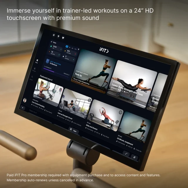 24-inch touchscreen mounted on a stand displaying iFIT workout thumbnails in a gym setting, with trainer-led videos visible on the screen